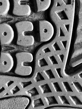 A close-up view of a textured surface, featuring a pattern of geometric shapes like circles and triangles. The material appears rubbery, with a detailed tread design suggesting it might be the sole of a shoe.