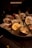 A plate of fresh oysters served on a bed of ice, accompanied by lemon wedges and small metal containers with condiments. The scene is dimly lit, giving it a warm, intimate dining atmosphere.