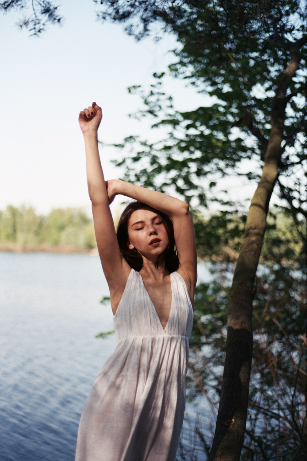 a woman standing next to a tree near a body of water