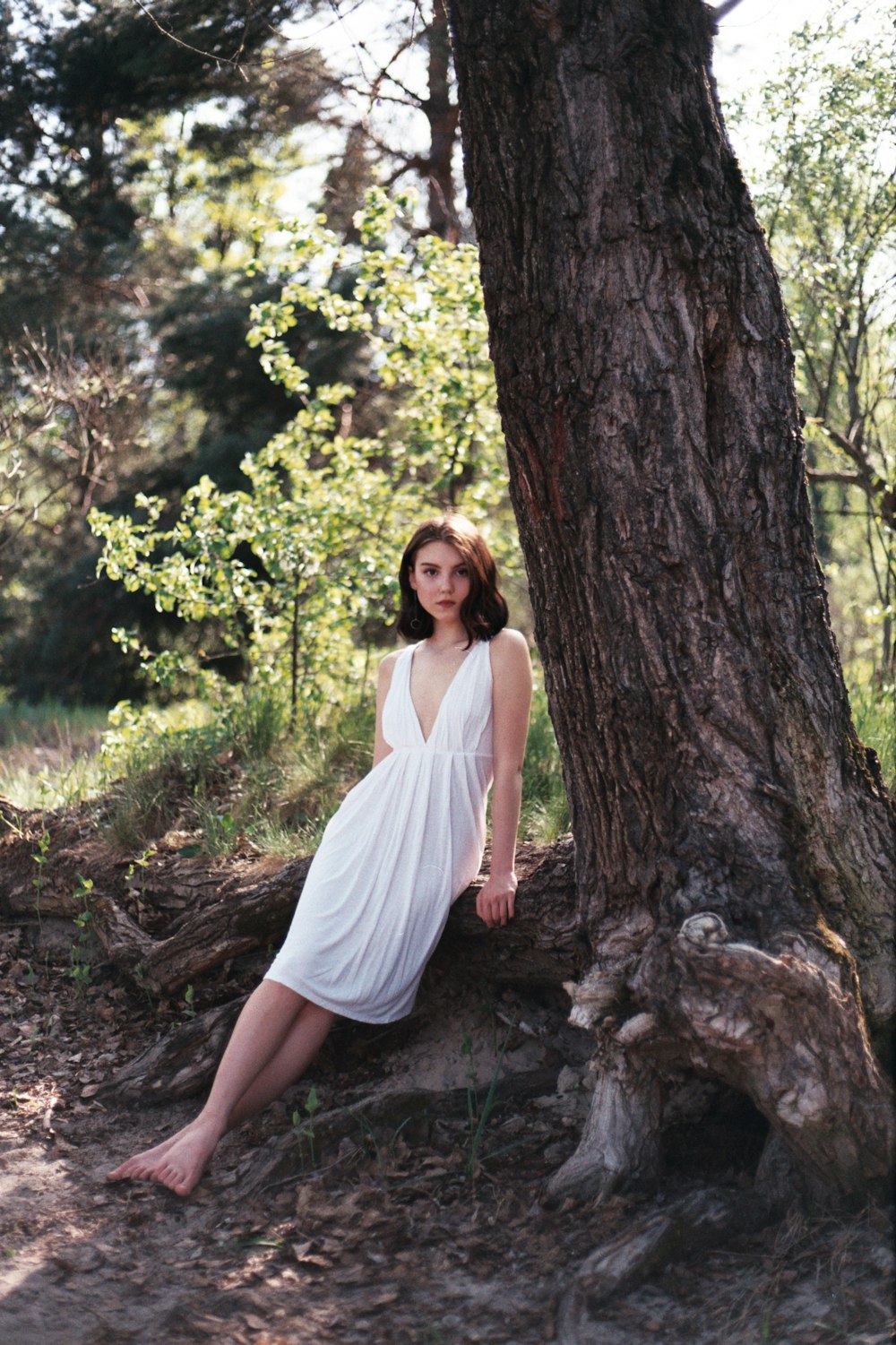 a woman in a white dress leaning against a tree