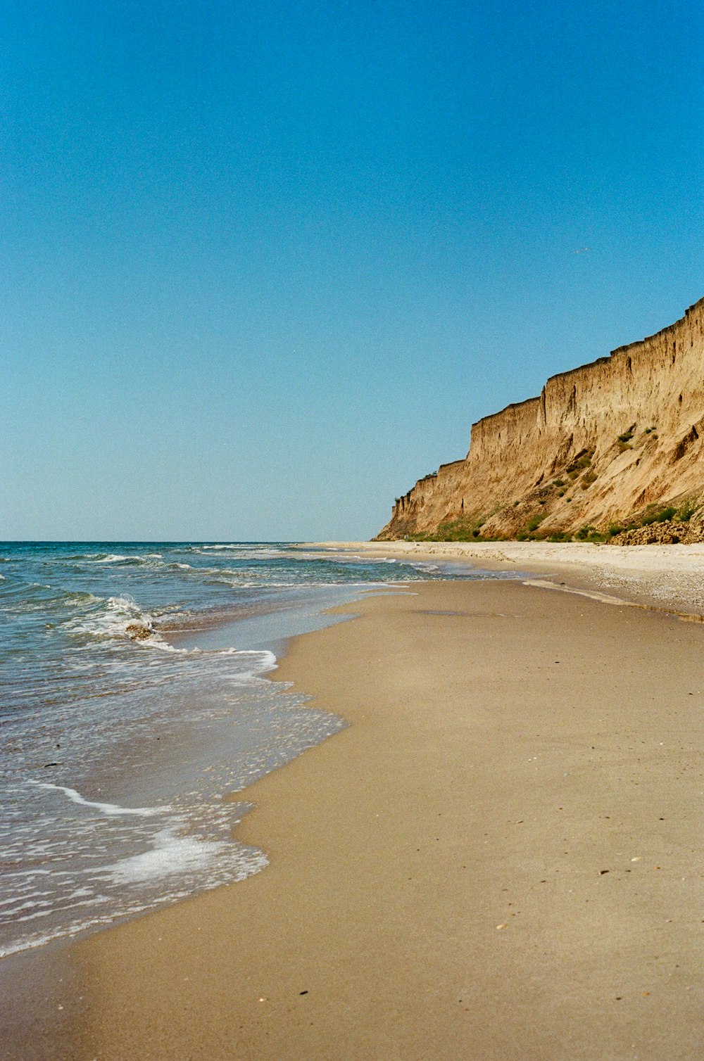 a sandy beach next to a cliff on a clear day