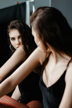 a woman sitting on a bed looking at herself in the mirror