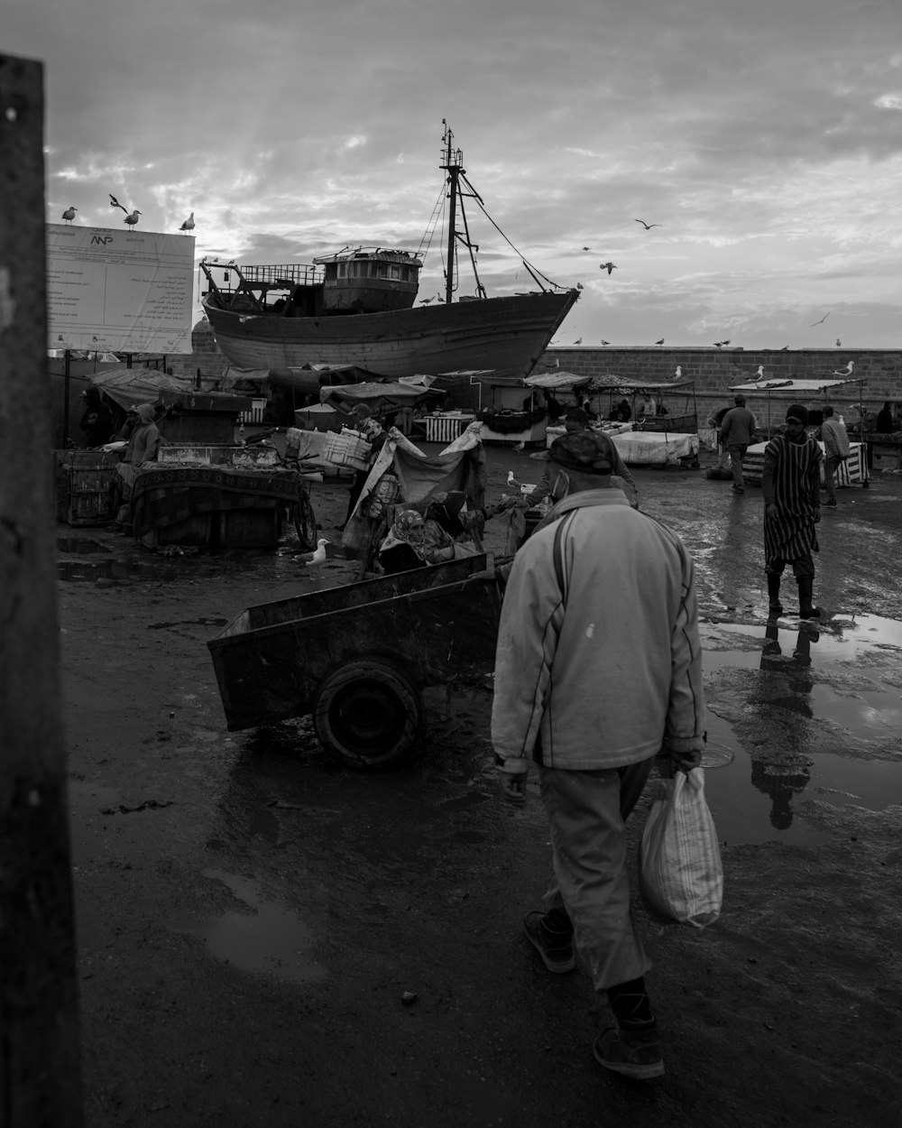 ein Schwarz-Weiß-Foto von Menschen, die in der Nähe eines Bootes spazieren gehen