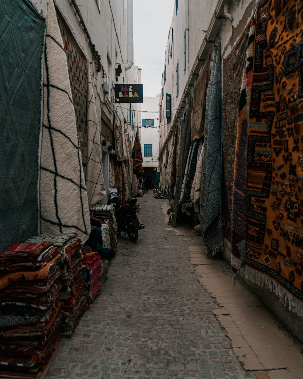 a narrow alleyway with carpets and rugs on the sides