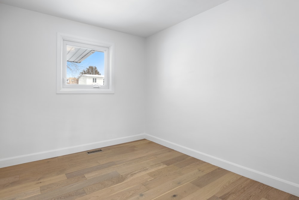 an empty room with a window and hard wood floor