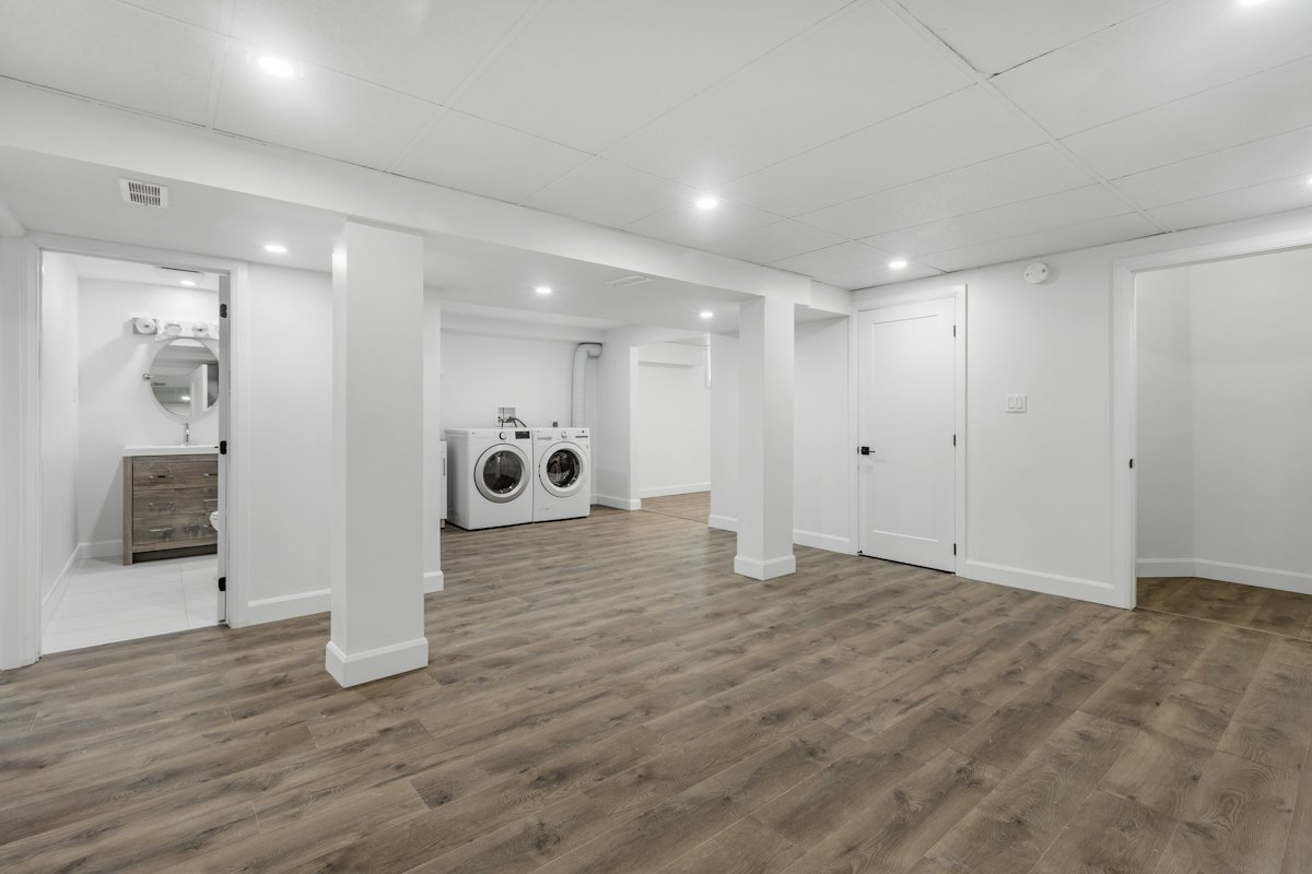 Finished basement with vinyl plank flooring, pot lights and a laundry area