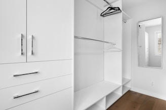 a walk in closet with white cabinets and drawers