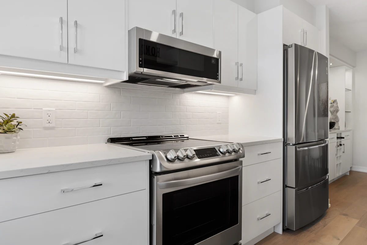 A white kitchen with a quartz countertop, a stainless steel stove, a microwave above it and a fridge.