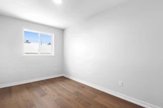 an empty room with a window and hard wood floor