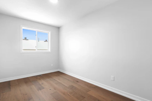 an empty room with a window and hard wood floor