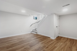 an empty room with a staircase and hard wood floors