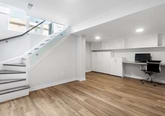 an empty room with a desk, computer, and stairs