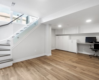 an empty room with a desk, computer, and stairs