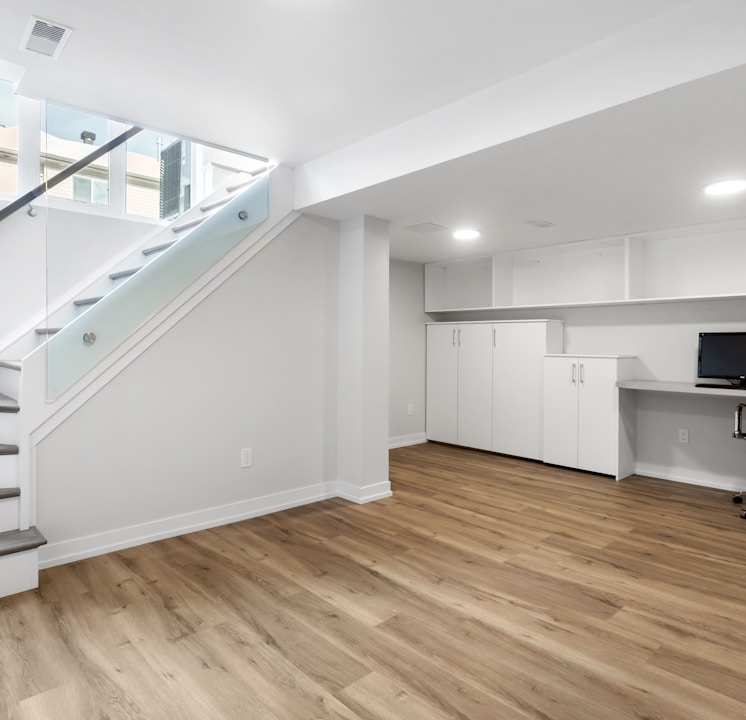 an empty room with a desk, computer, and stairs