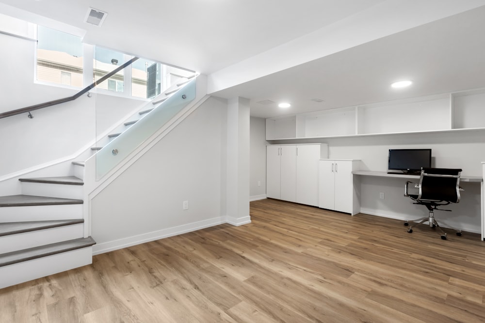 an empty room with a desk, computer, and stairs