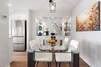 a dining room table with white chairs and a painting on the wall