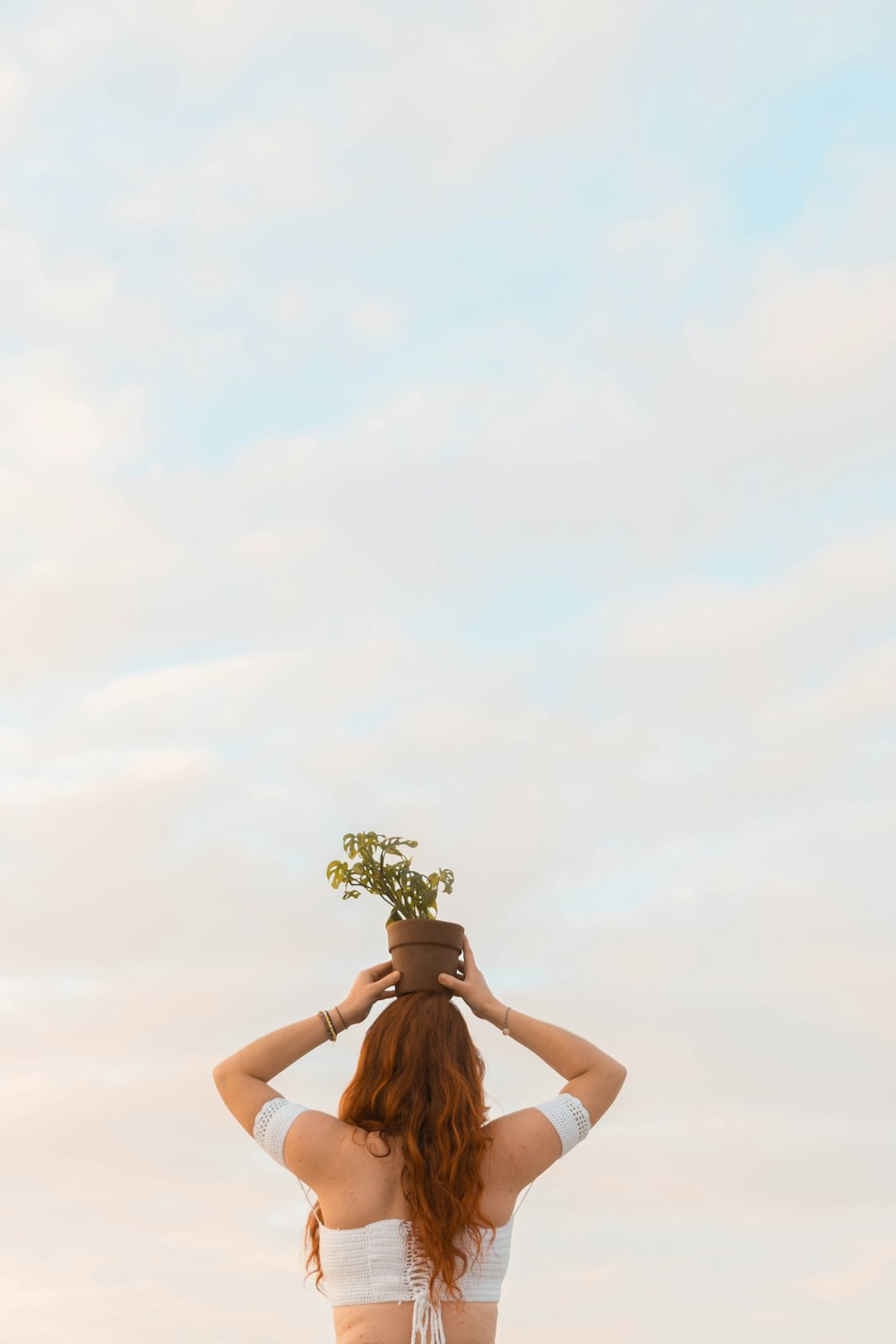 a woman in a bikini holding a potted plant on her head