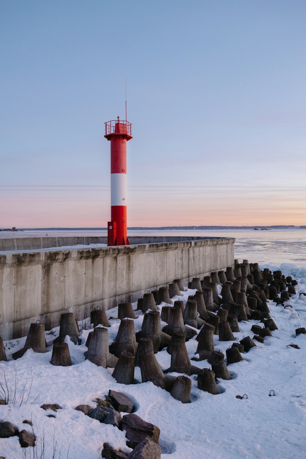 a red and white lighthouse sitting on top of a snow covered beach