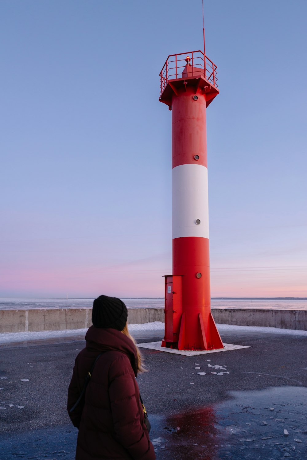 a woman standing in front of a red and white lighthouse