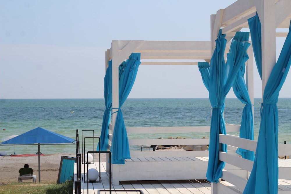 a gazebo on the beach with blue drapes on it