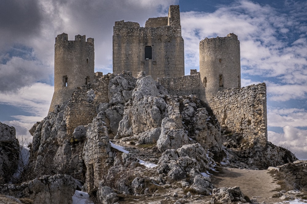 a castle on top of a rocky mountain under a cloudy sky