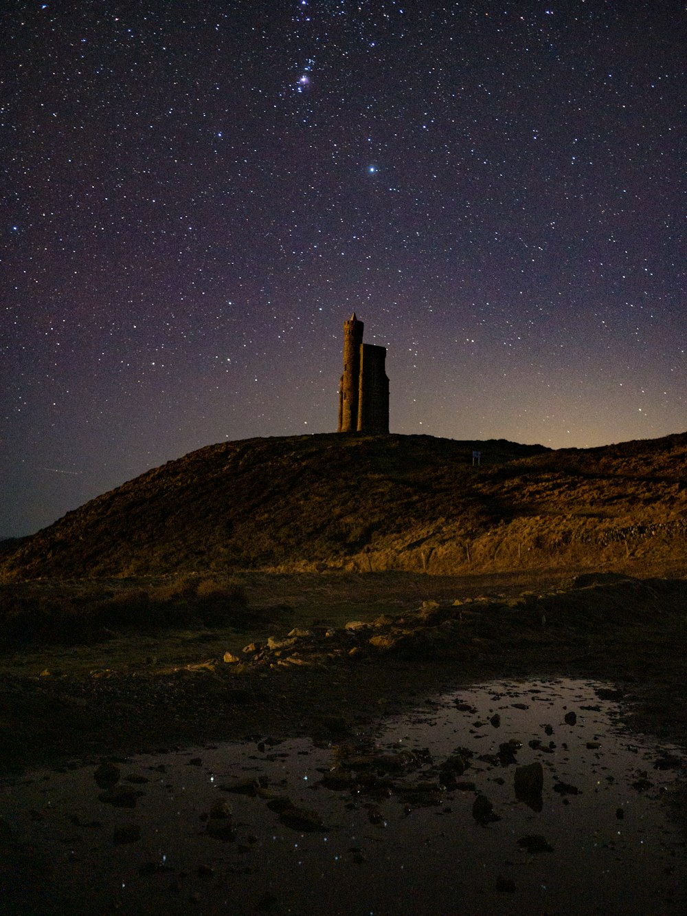 a tower on a hill with a sky full of stars