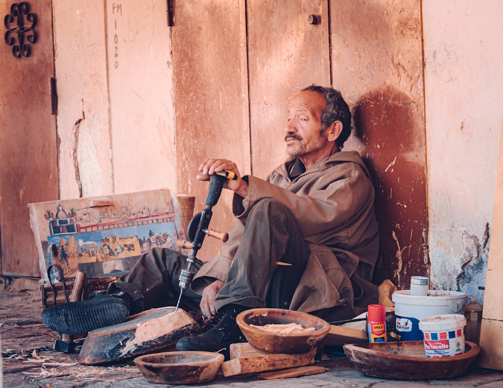 a man sitting on the ground next to a wooden wall