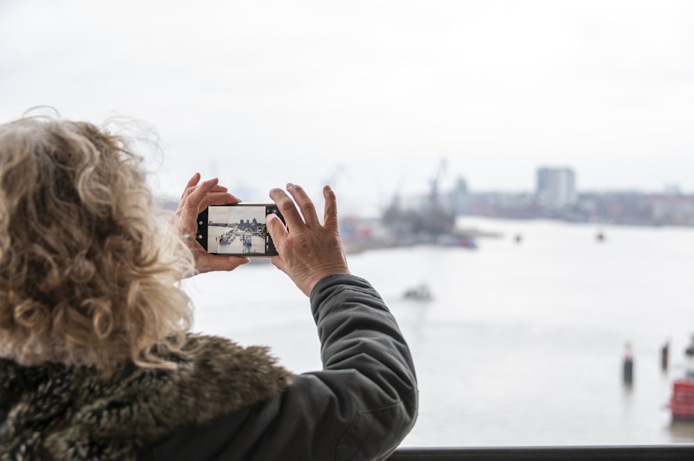 a woman taking a picture of a harbor with a cell phone