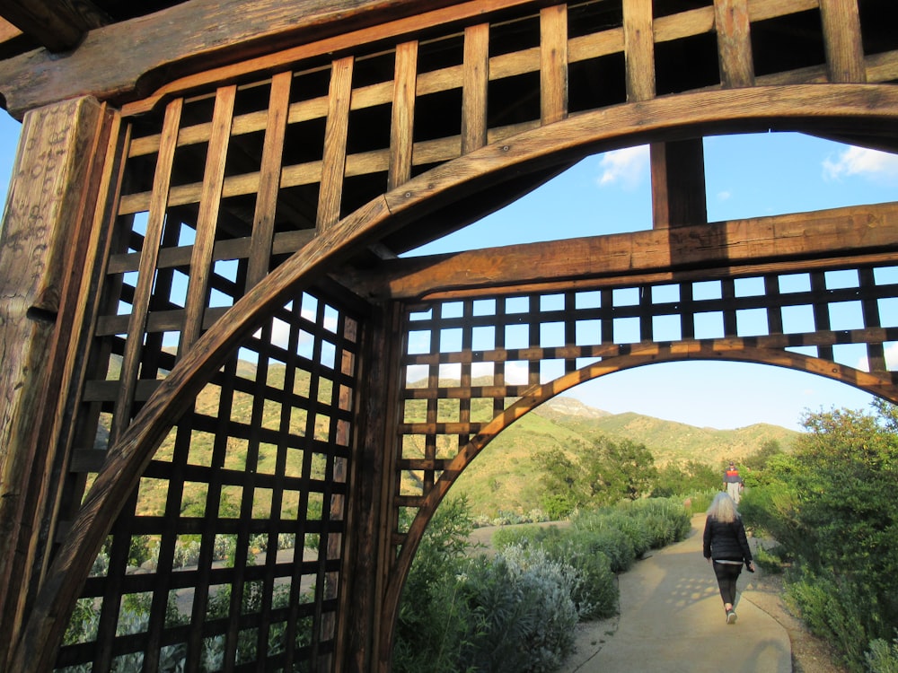 a woman walking down a path under a wooden structure