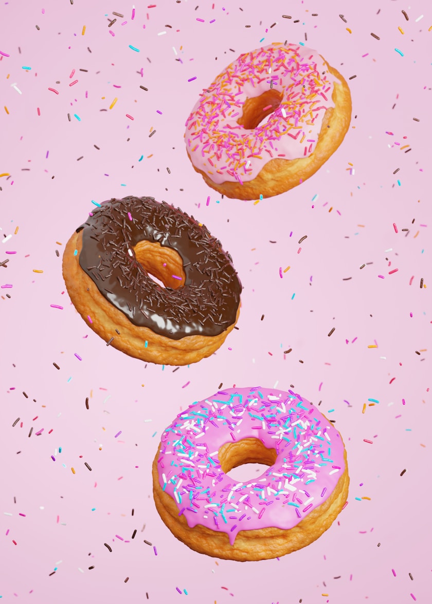 three donuts with pink frosting and sprinkles on a pink background