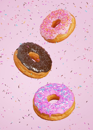 three donuts with pink frosting and sprinkles on a pink background