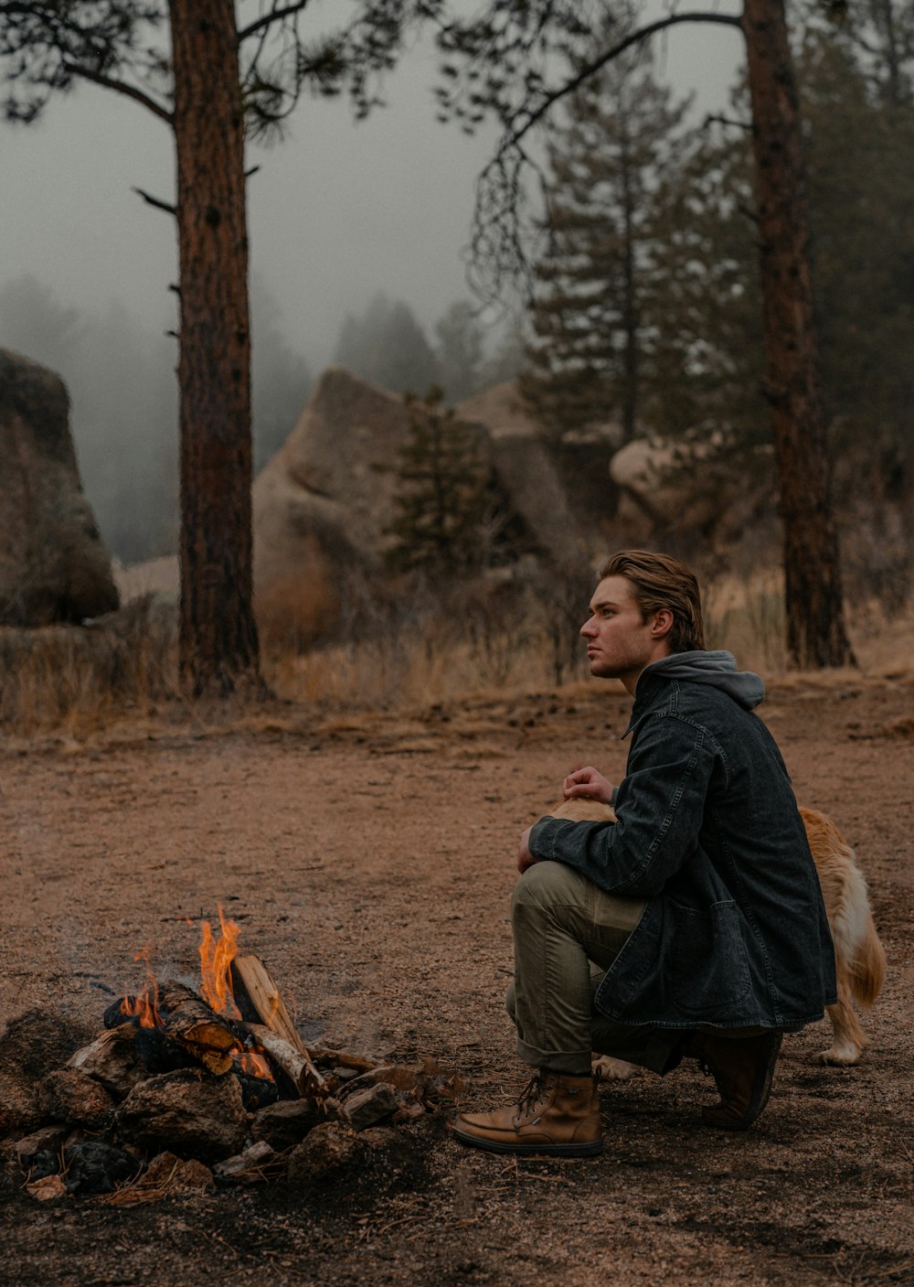 a man sitting in front of a campfire with his dog