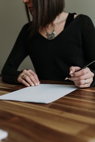 a woman sitting at a table writing on a piece of paper