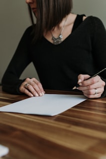 a woman sitting at a table writing on a piece of paper