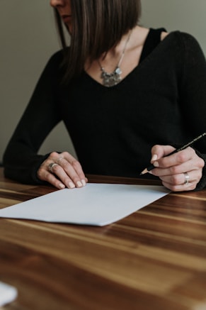 a woman sitting at a table writing on a piece of paper