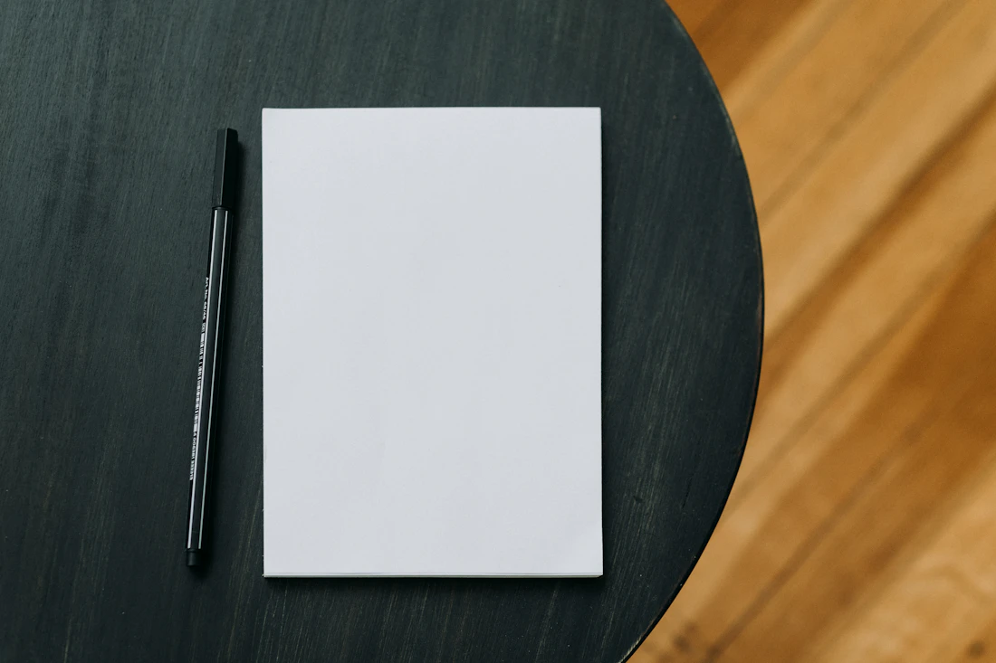 A blank notepad and a pen resting on a wooden table