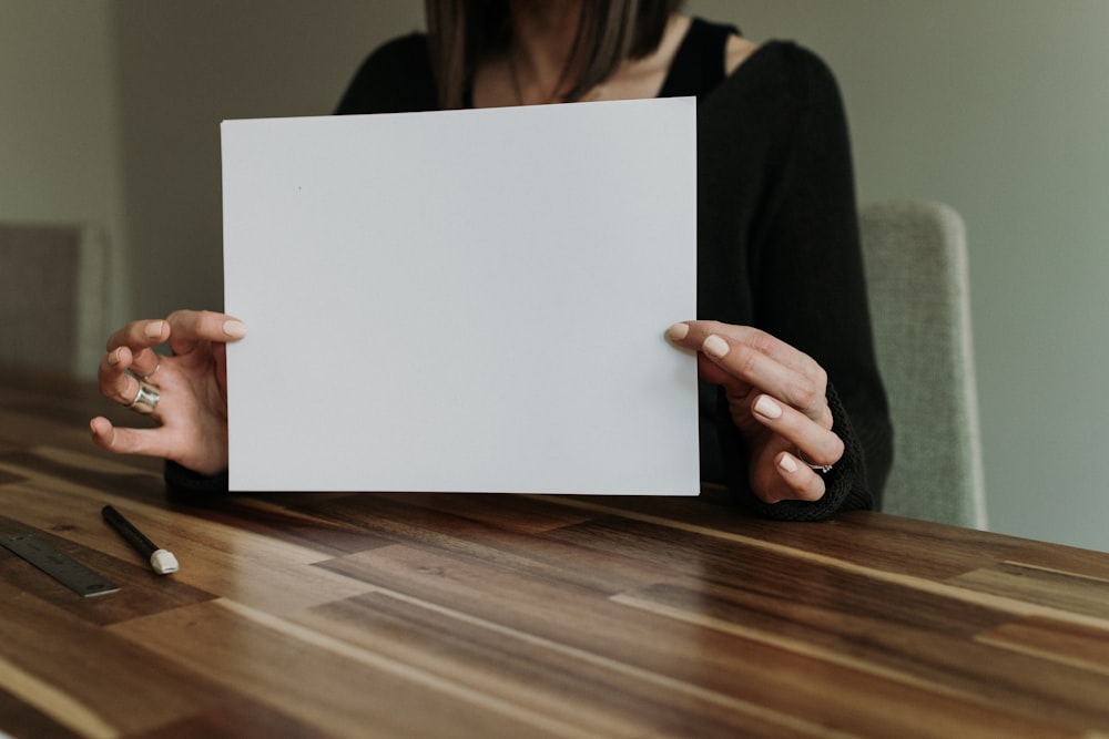 a woman holding a piece of paper on top of a wooden table