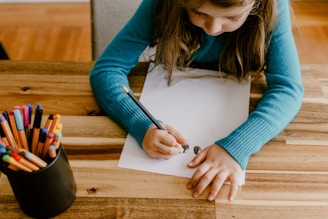 a young girl sitting at a table with colored pencils