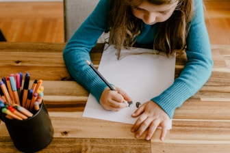 a young girl sitting at a table with colored pencils