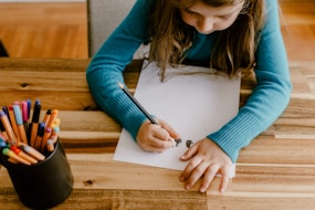 a young girl sitting at a table with colored pencils