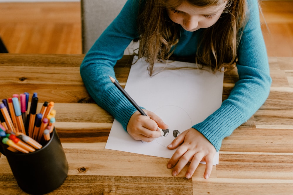 a young girl sitting at a table with colored pencils