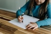 a young girl sitting at a table writing on a piece of paper