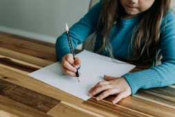 a young girl sitting at a table writing on a piece of paper