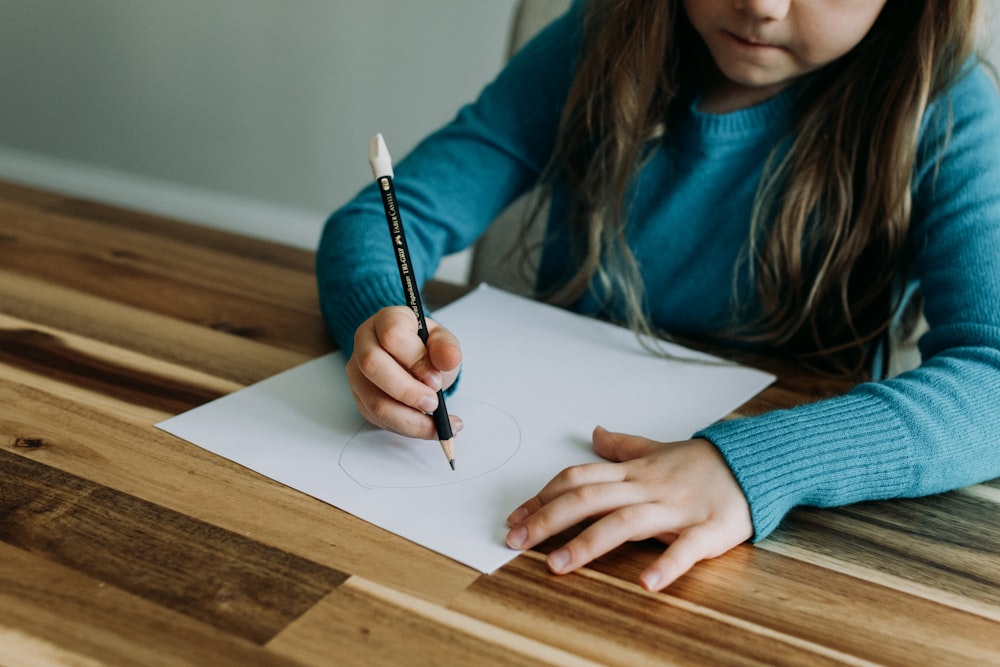 a young girl sitting at a table writing on a piece of paper