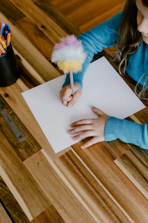 a little girl sitting at a table with a piece of paper and a brush