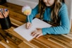 a little girl sitting at a table writing on a piece of paper