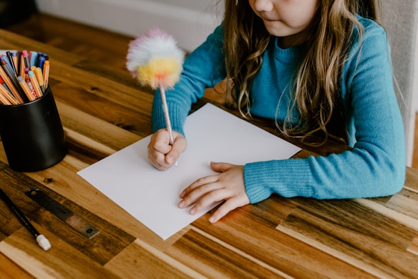 a little girl sitting at a table writing on a piece of paper