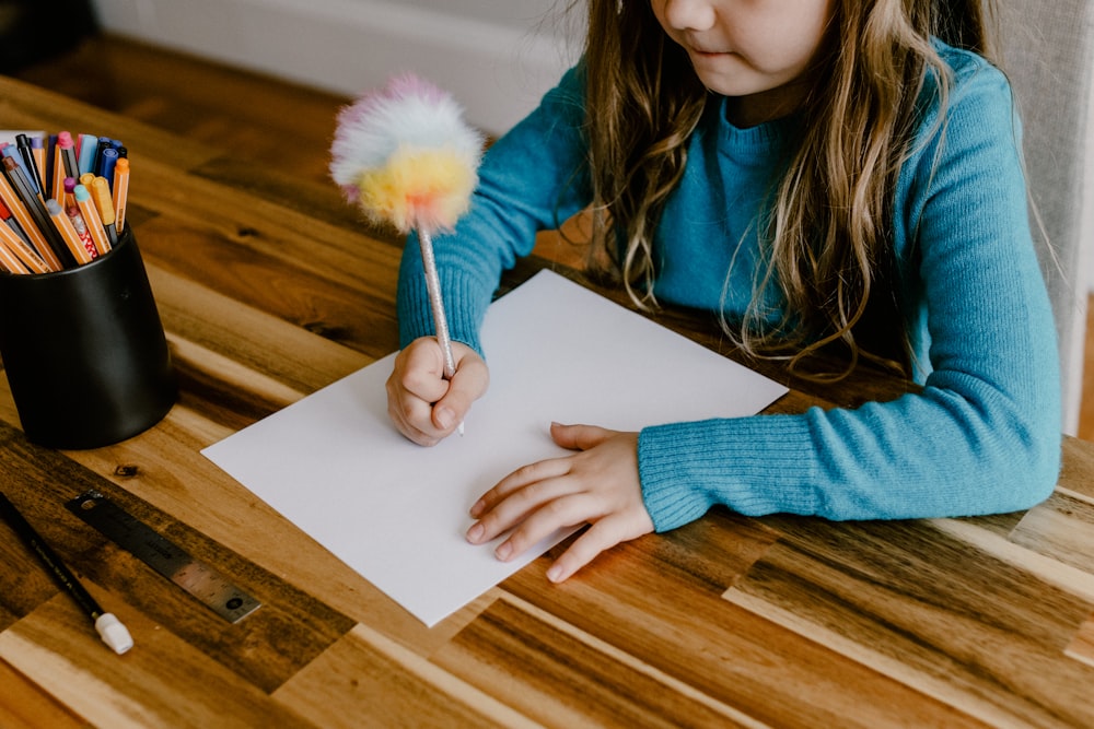 a little girl sitting at a table writing on a piece of paper