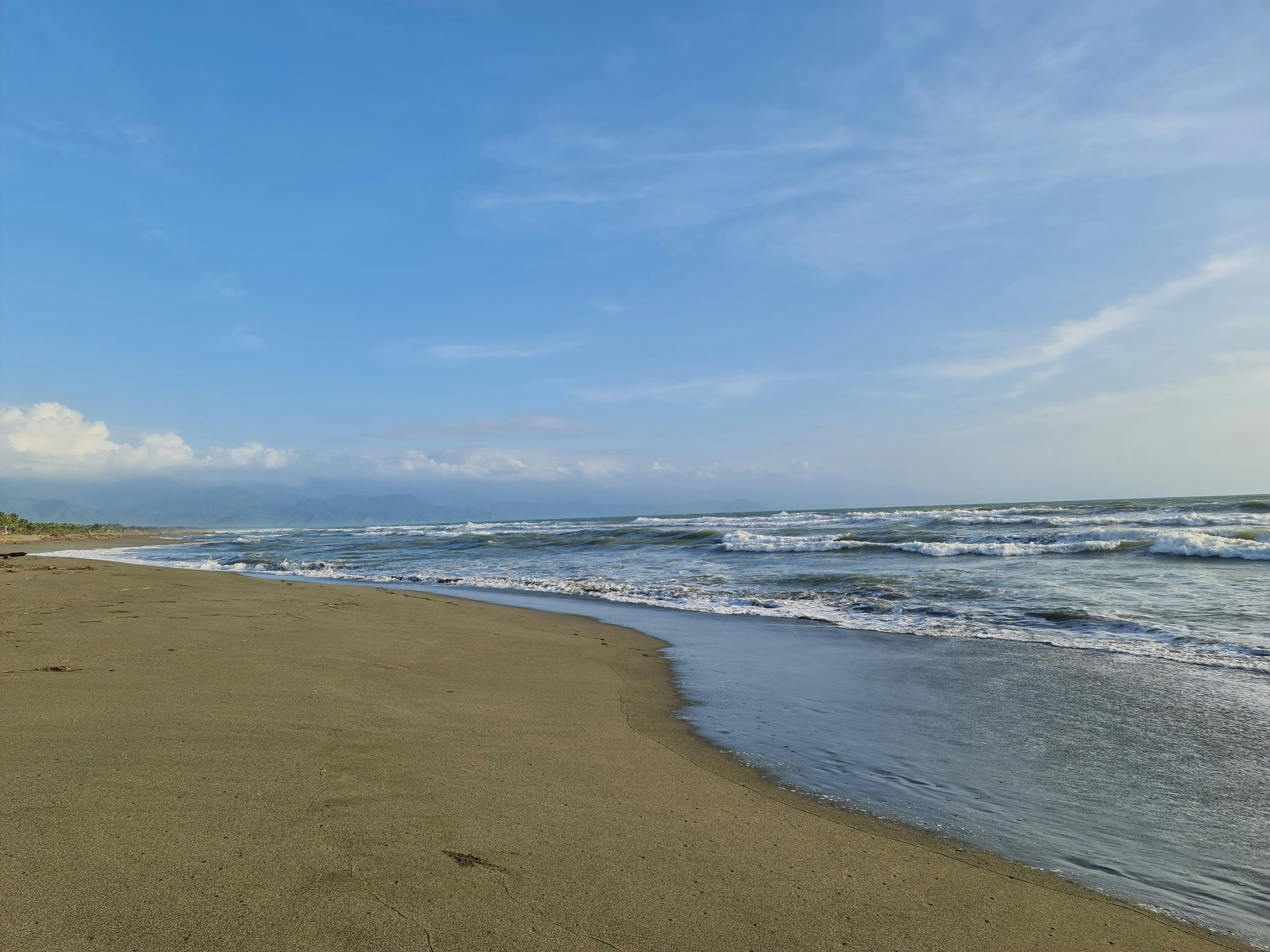 a sandy beach next to the ocean under a blue sky