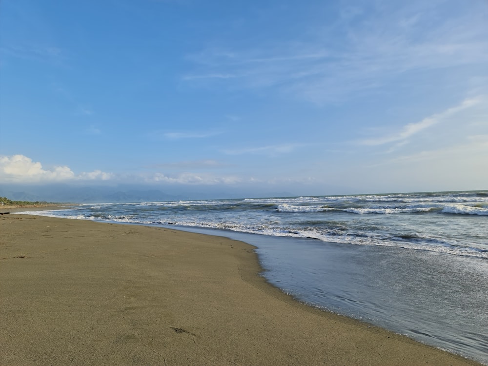 a sandy beach next to the ocean under a blue sky